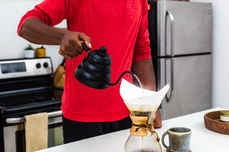 Image of a man hand pouring and brewing speciality coffee at home using a pouring kettle and a Chemex coffee maker.